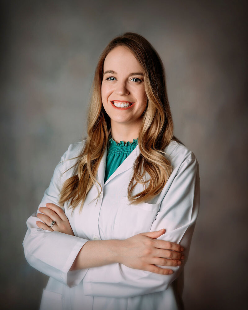 Portrait of a young white woman wearing a white lab coat with a turquoise shirt underneath.