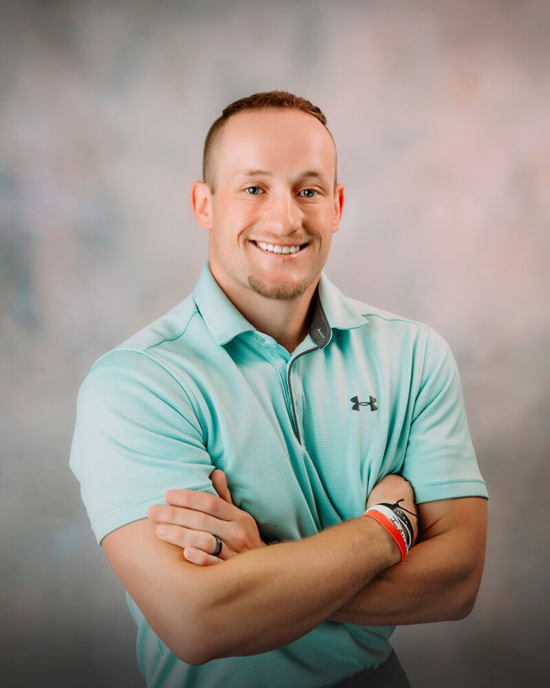 Vertical portrait of a white man wearing a teal shirt crossing his arms